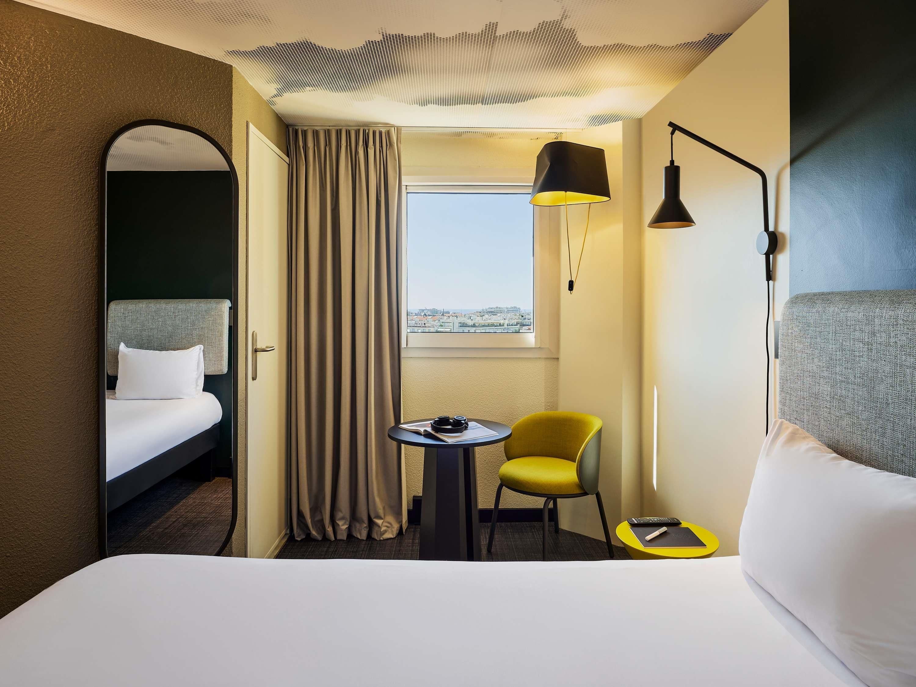 Une chambre d’hôtel avec un lit, une petite table et une chaise, une fenêtre donnant sur un paysage agréable et une lampe.