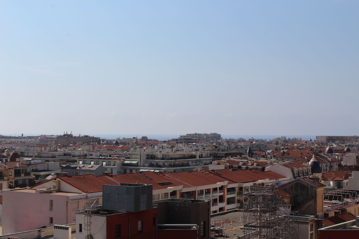 A cityscape with densely packed buildings, some with red-tiled roofs, and a clear sky.