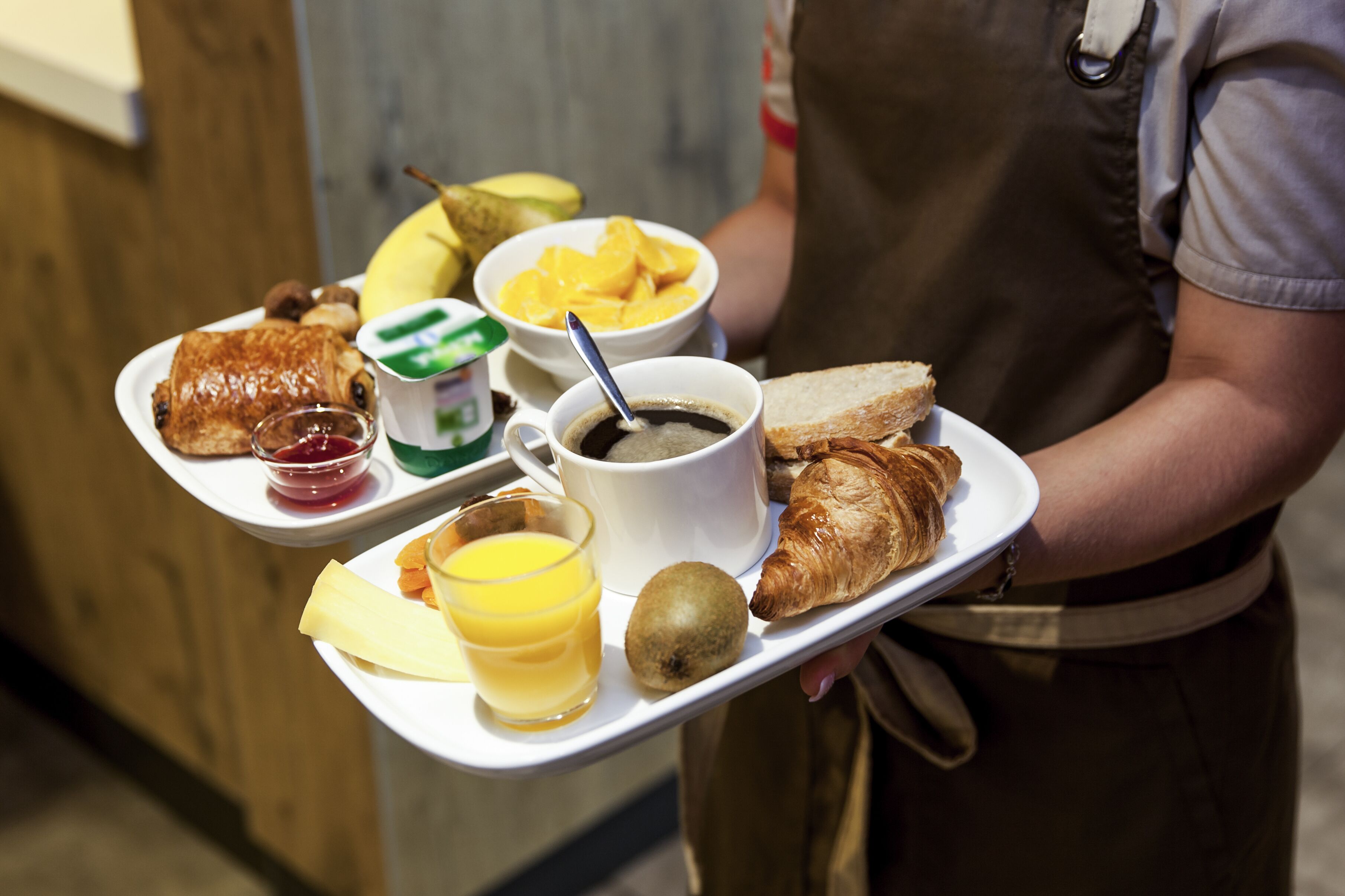 A tray with breakfast items including toast, croissant, kiwi, orange juice, coffee, and a bowl of mango slices.