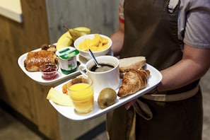 A tray with breakfast items including toast, croissant, kiwi, orange juice, coffee, and a bowl of mango slices.