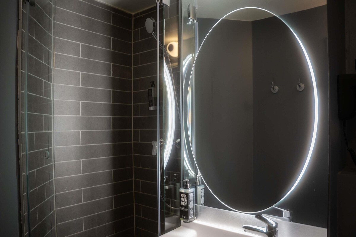 A bathroom with a large mirror, a sink, and a shower area.