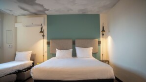 Habitación de hotel con una cama grande, dos mesitas de noche, aire acondicionado instalado en la pared y dos lámparas murales.