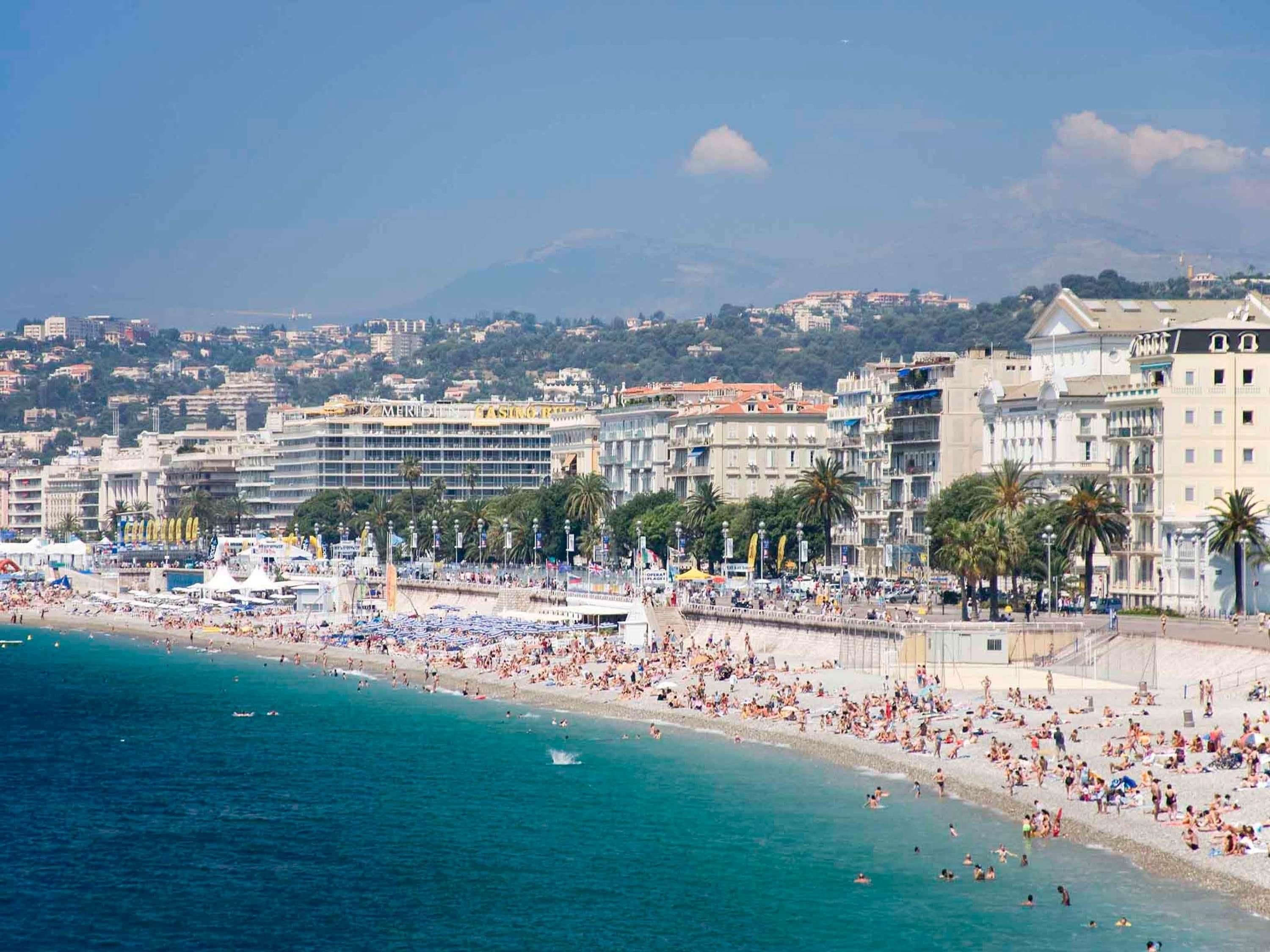 Un paisaje urbano costero con una playa concurrida, edificios y una montaña al fondo.