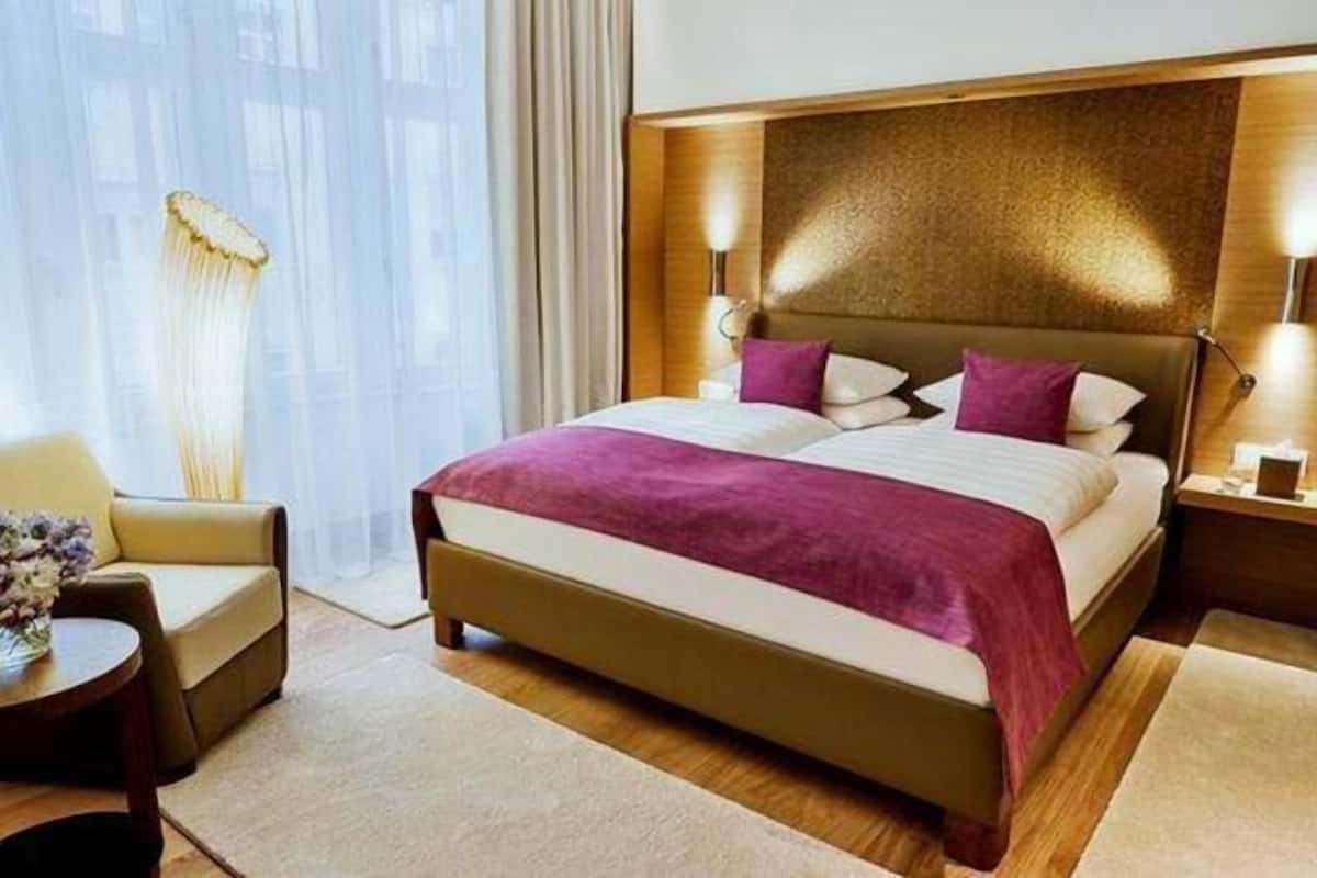 Een hotelkamer met een bed, nachtkastje, stoel en een raam met gordijnen.