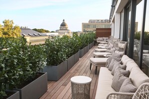 Terraço no telhado com sofá, cadeiras e plantas em vasos.