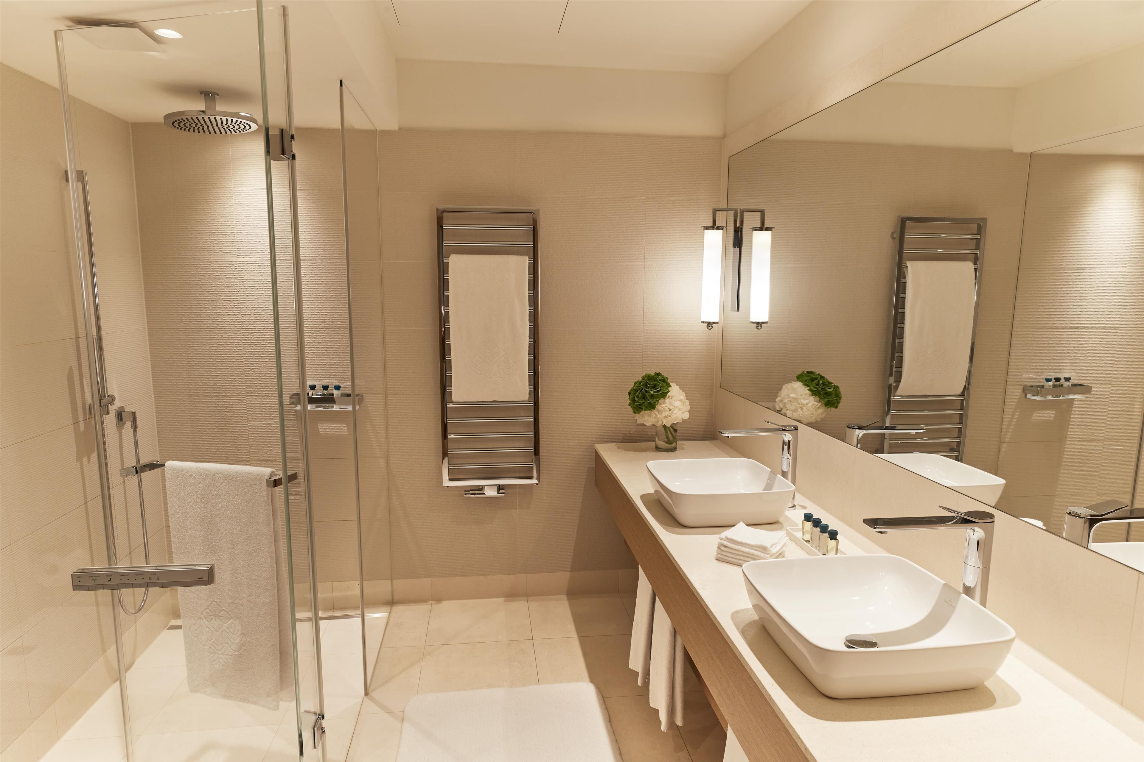 Une salle de bain moderne avec une douche à l’italienne en verre, un long meuble-lavabo doté de deux vasques et un grand miroir.