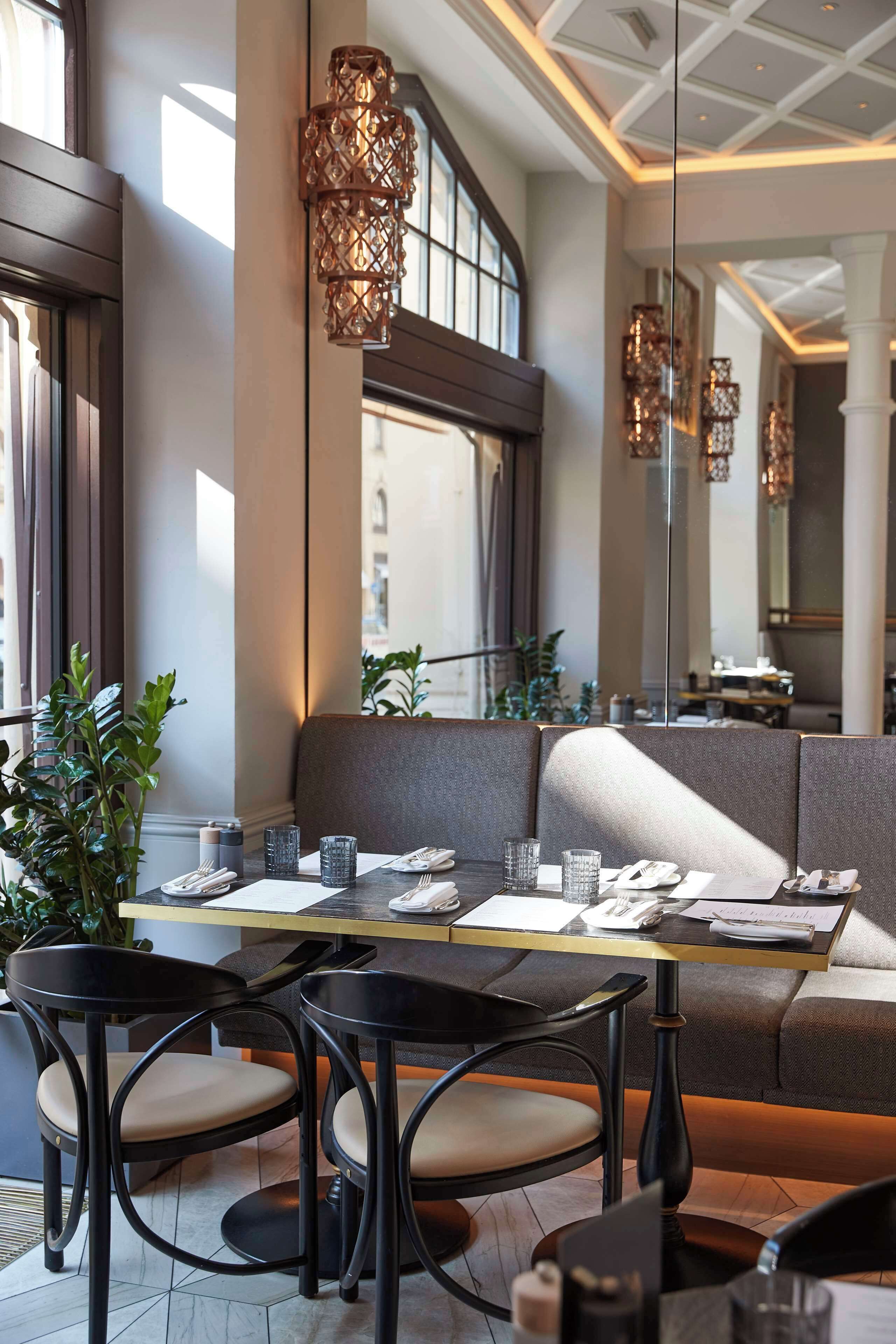 A modern dining area with a long table, cushioned seating, and decorative lighting.