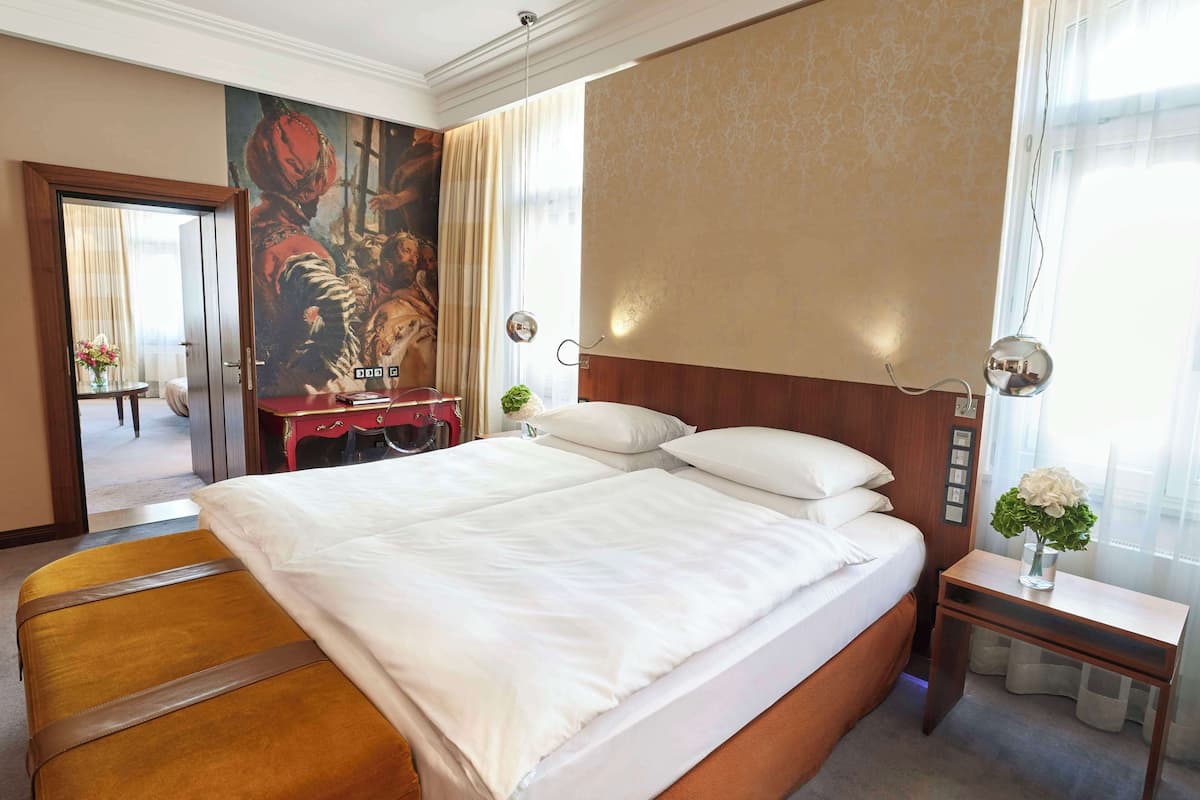 Une chambre d’hôtel avec un grand lit, une table de chevet en bois ornée d’un vase de fleurs, un bureau avec une chaise et un tableau accroché au mur.