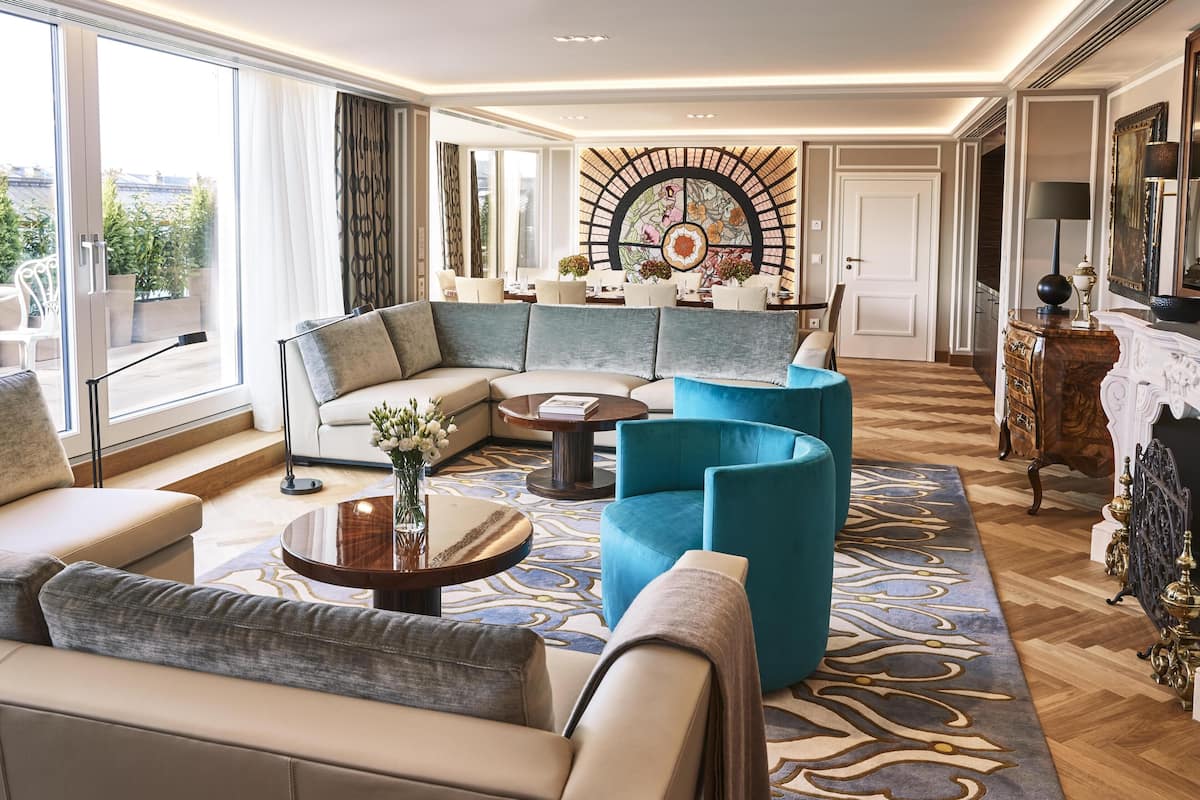 Un salon moderne avec un canapé d’angle, un fauteuil bleu, une table basse et un élément décoratif mural.