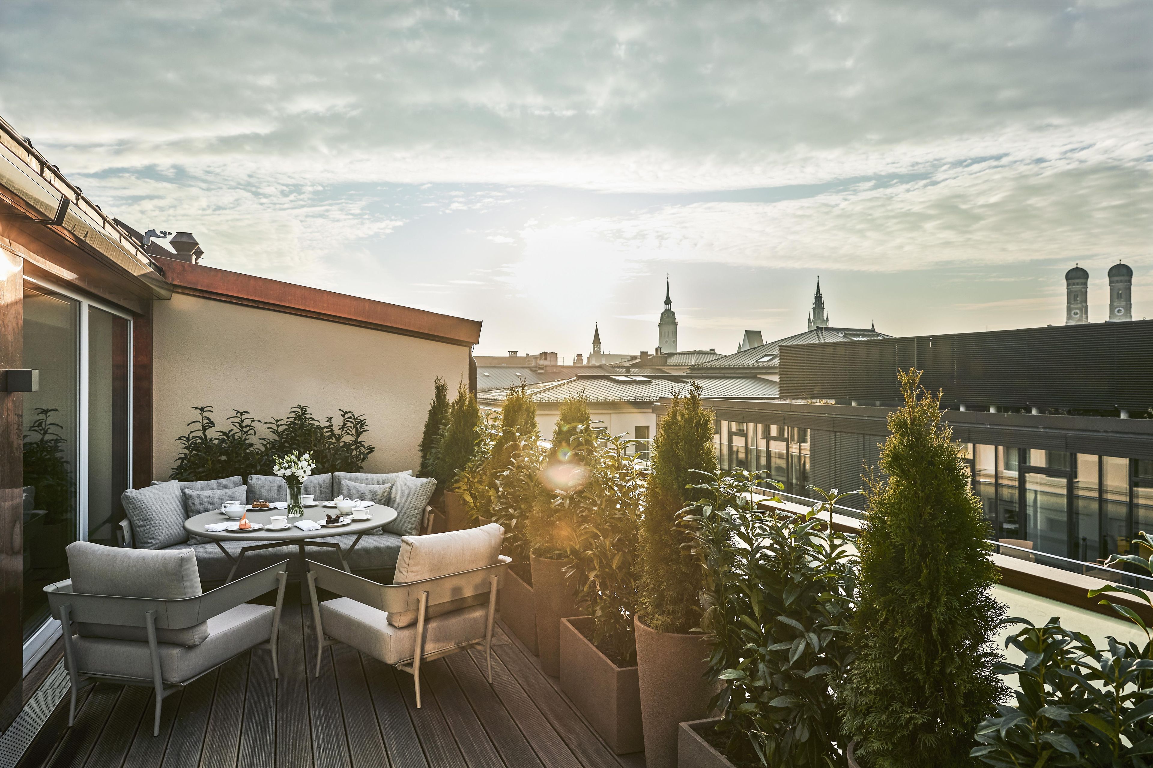 A rooftop terrace with a seating area, potted plants, and a view of city buildings.