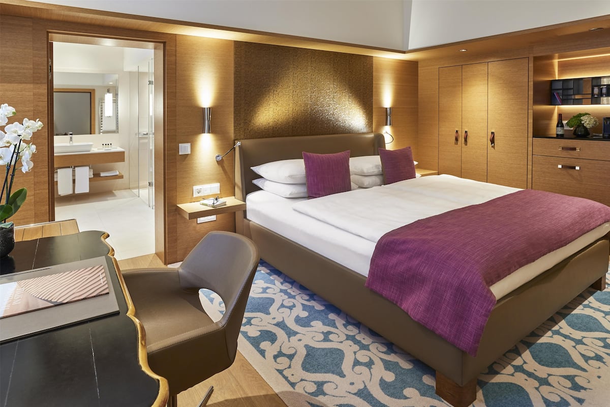 Une chambre d’hôtel moderne, dotée d’un grand lit, d’un bureau, d’une chaise et d’une salle de bain visible à travers une porte ouverte.