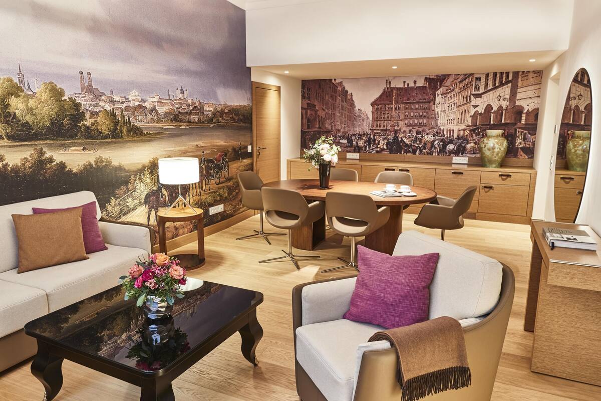 Une chambre d’hôtel moderne avec une grande fresque représentant un paysage urbain, un coin repas et un espace salon confortable.