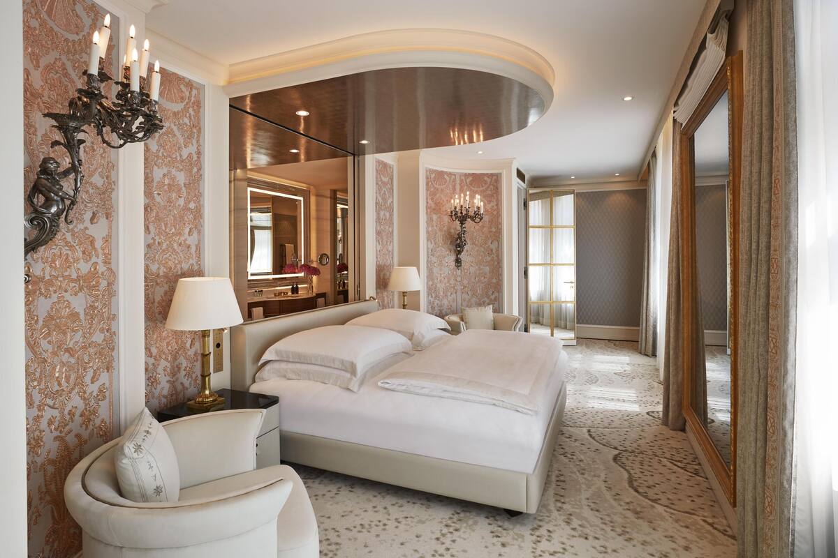 Une chambre spacieuse avec un grand lit, deux tables de chevet, un miroir et un lustre.