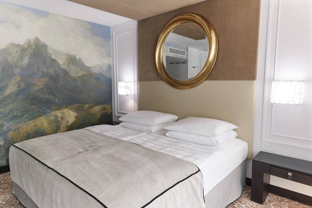 Une chambre d’hôtel avec un grand lit, un tableau au mur, un miroir rond et une table de chevet.