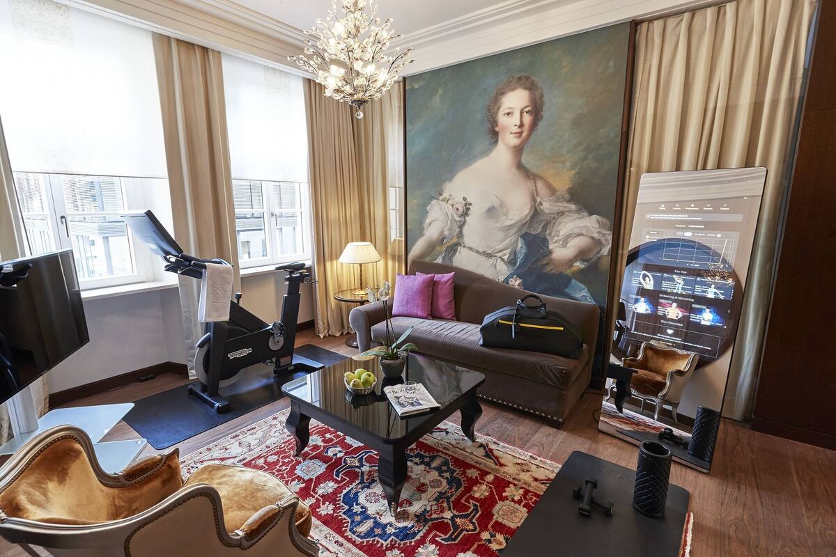 Habitación de hotel con un ventanal grande, una cinta de correr, un sofá, una mesa de centro, una silla y un cuadro.