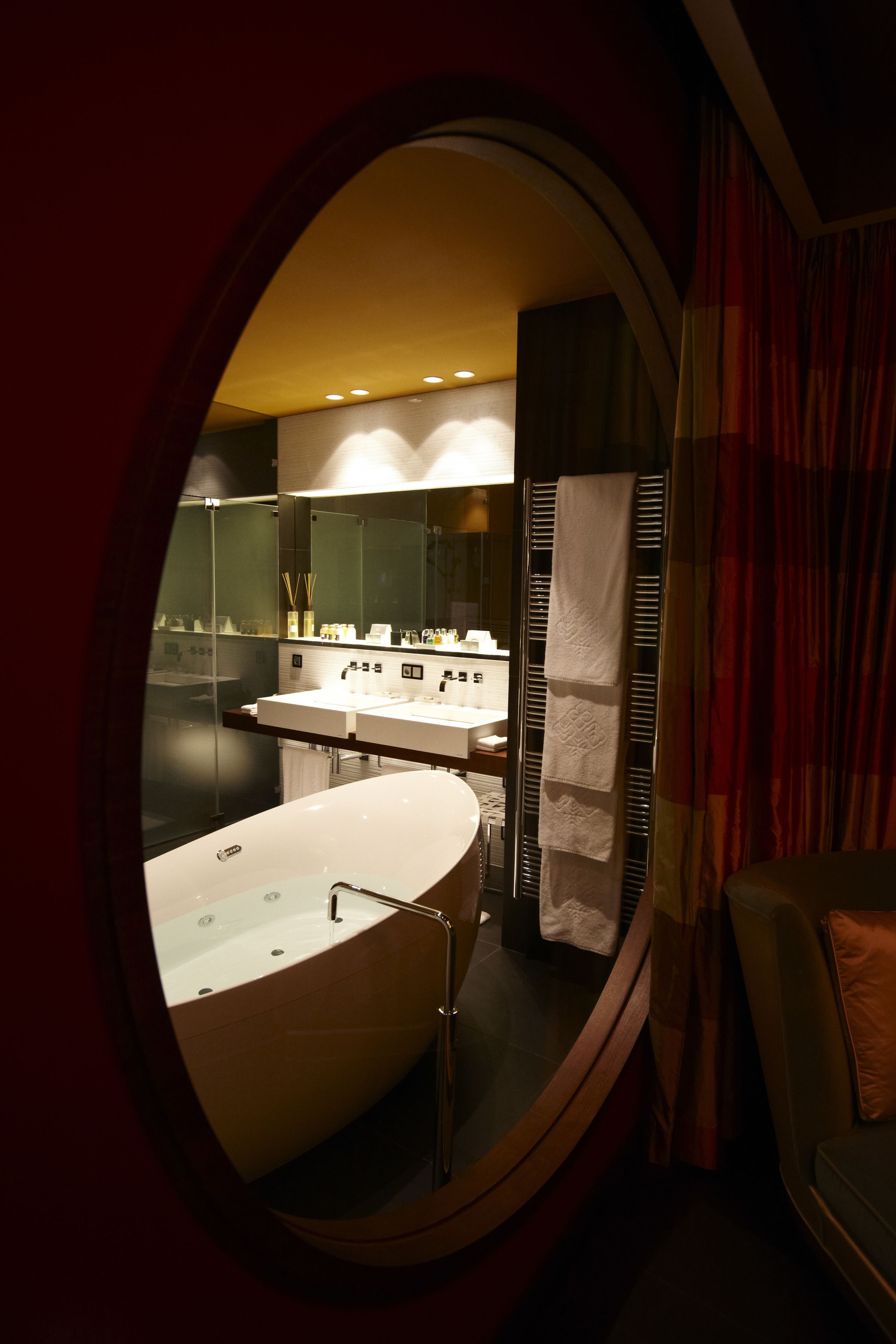 A modern bathroom with a large oval mirror, a freestanding bathtub, and a vanity with a mirror.