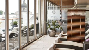 Ein moderner Lounge-Bereich mit großen Fenstern, einer Zimmerpflanze und einem Schild mit der Aufschrift 'Fitness'.