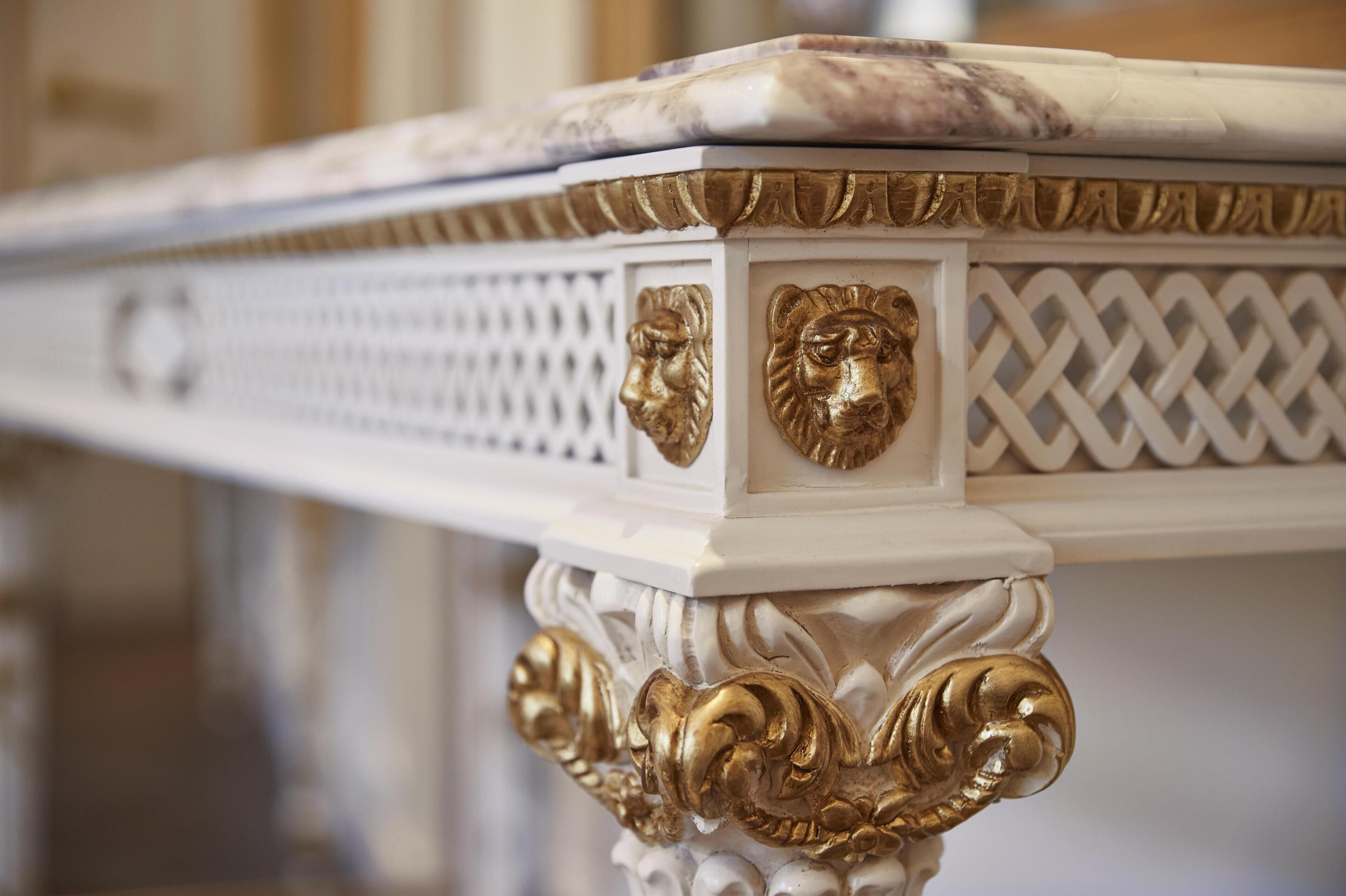 A close-up of a white marble table with gold accents and decorative lion heads.