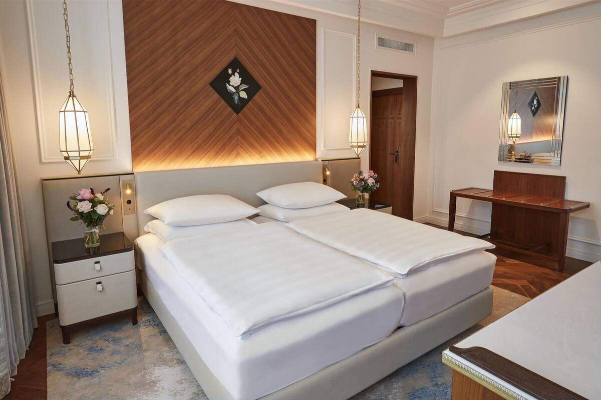 Une chambre d’hôtel avec un grand lit, des tables de chevet, une petite table, un miroir et un mur décoratif en bois.