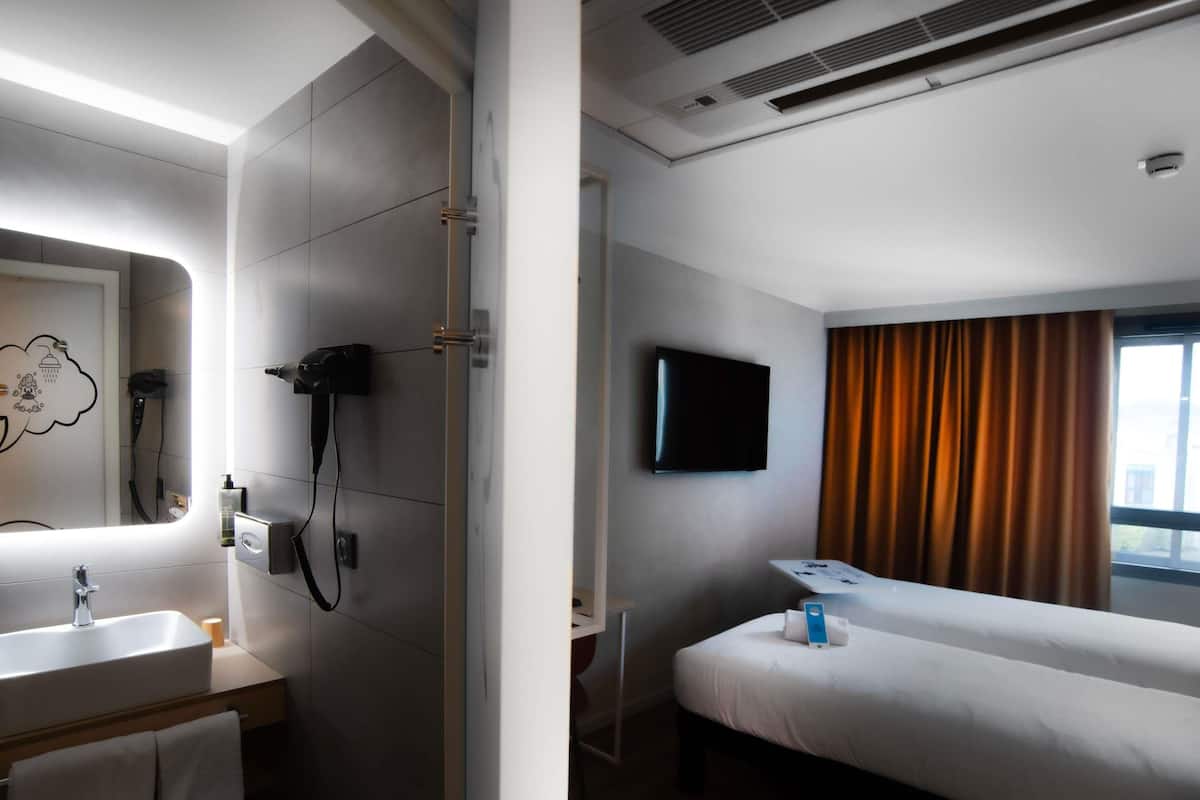 A hotel room with a bathroom, a bed, a TV, and a window with curtains.