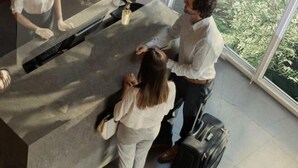 A reception desk with a glass partition, a computer, and a small table with a bottle. There is a suitcase on the floor and a person standing by the desk. - ibis Styles Clermont Ferrand Le Brezet Aeroport (Clermont-Ferrand)