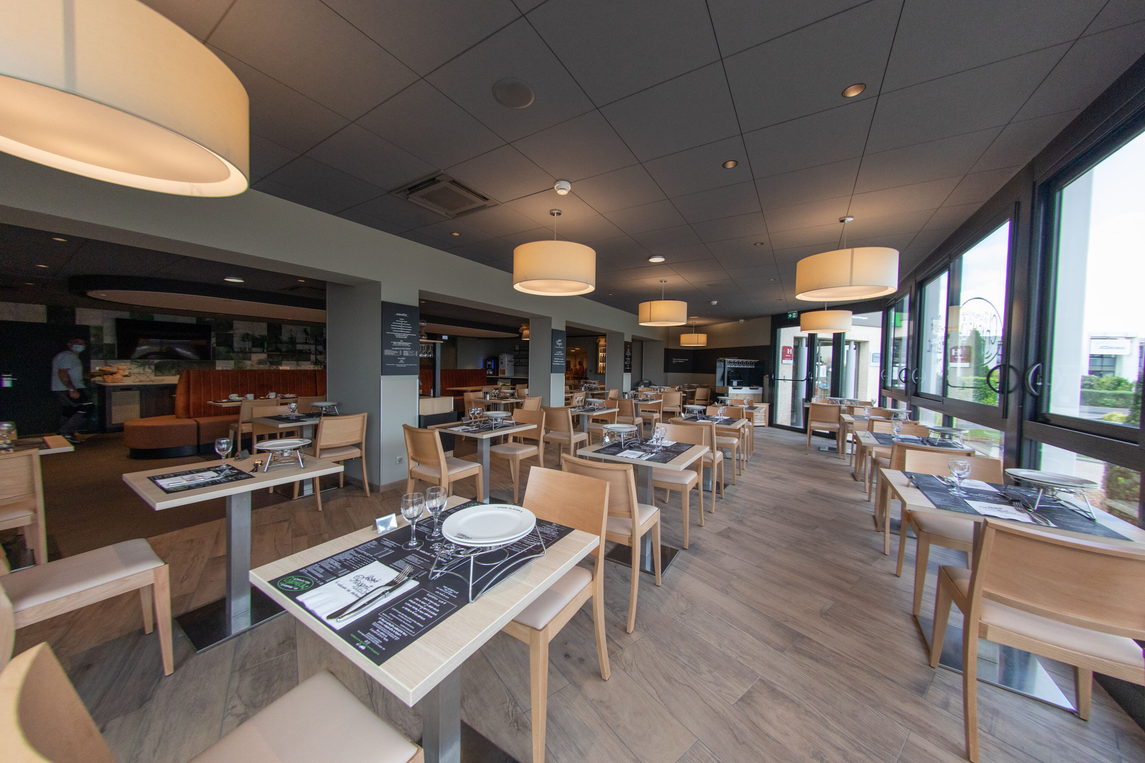 A spacious restaurant with multiple dining tables, wooden chairs, and pendant lighting.