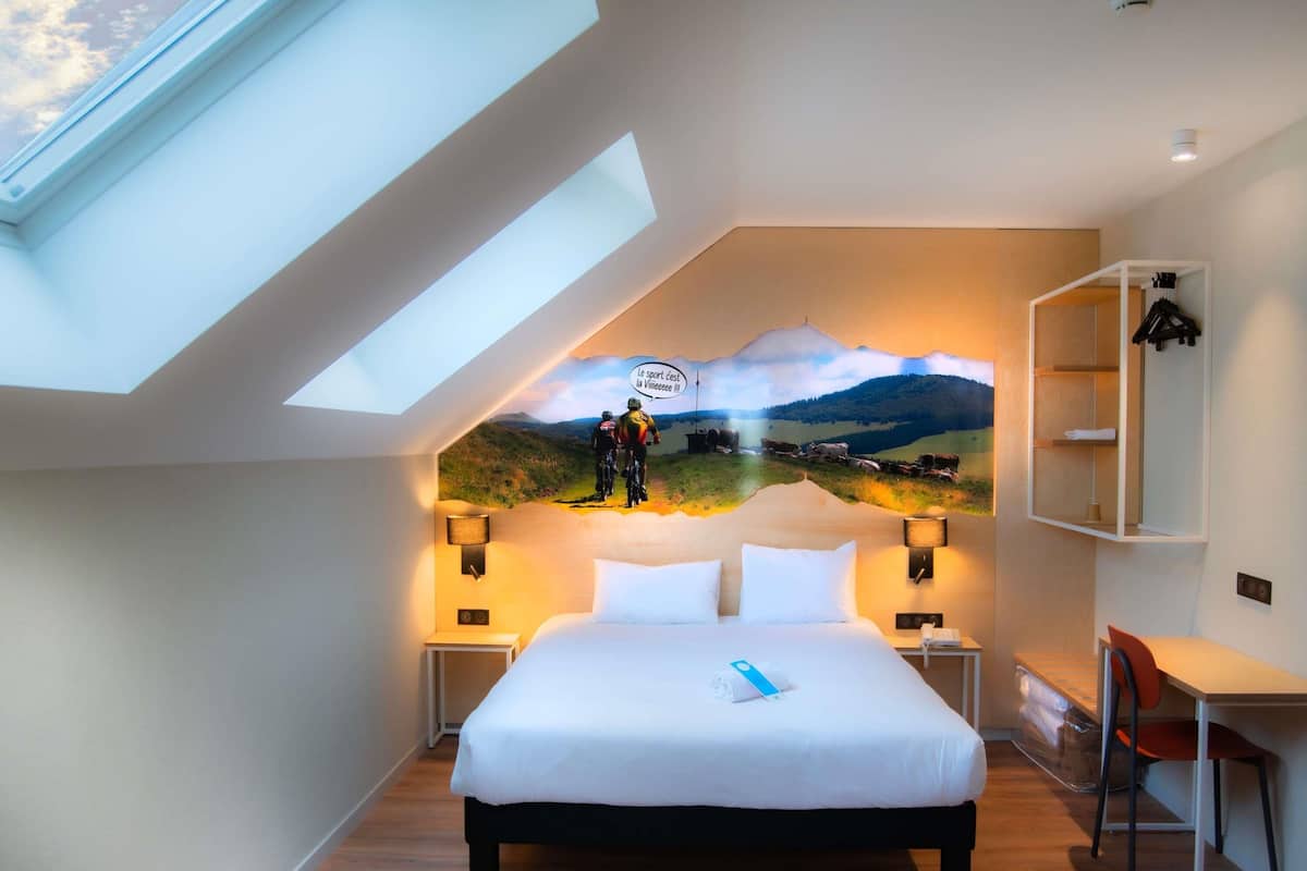 A bedroom with a bed, a desk, a chair, and a skylight.
