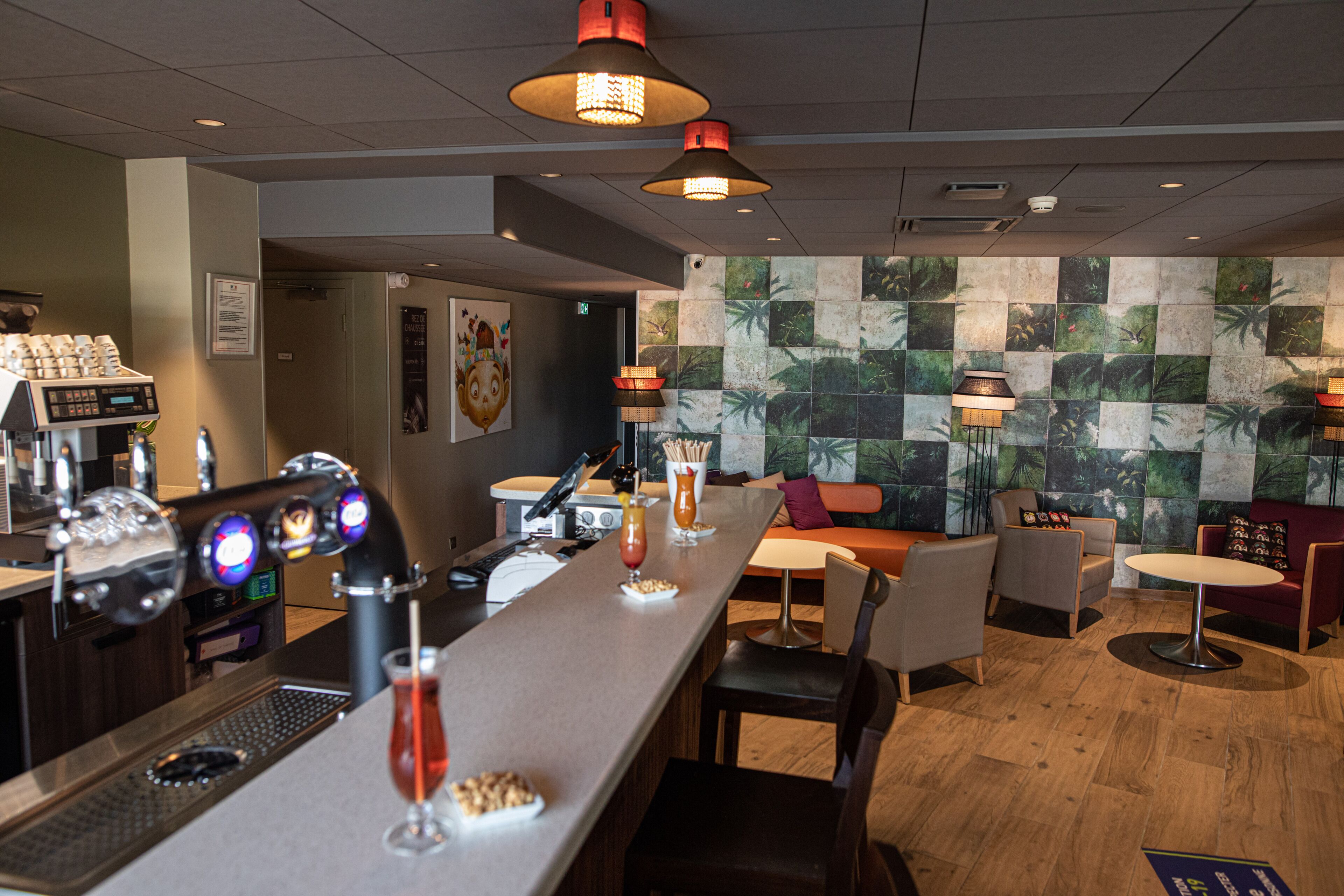 A bar area with a coffee machine, bar stools, and a mural of tropical leaves on the wall.