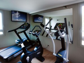 Ein Heim-Fitnessraum mit Laufband, Crosstrainer und Ergometer, ausgestattet mit digitalen Anzeigen.