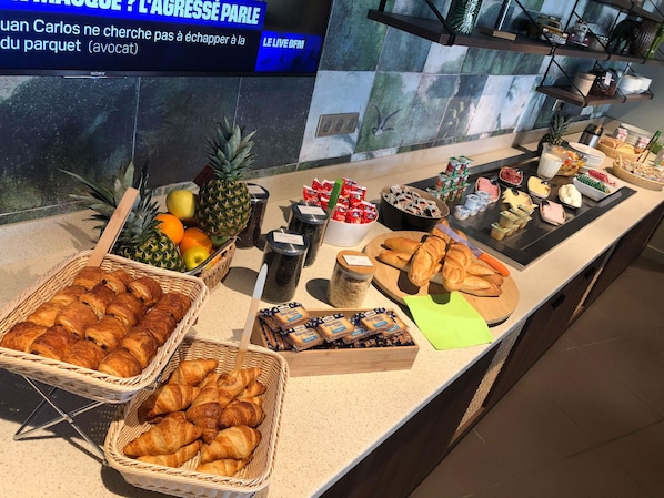 Un buffet proposant une variété de plats, notamment des fruits, des pùtisseries et des condiments.