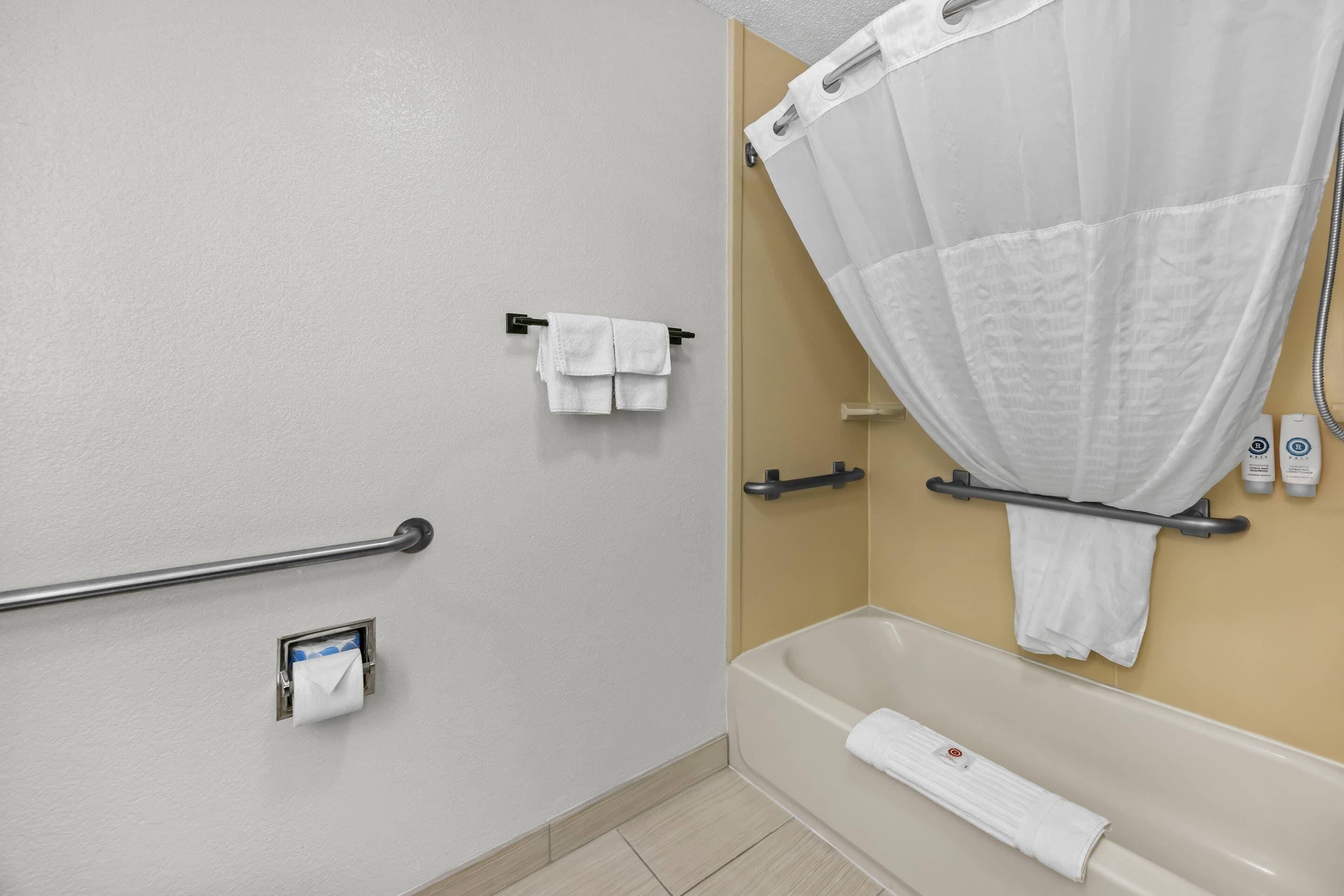 Un baño con bañera, cortina de ducha, toallero y barandilla.