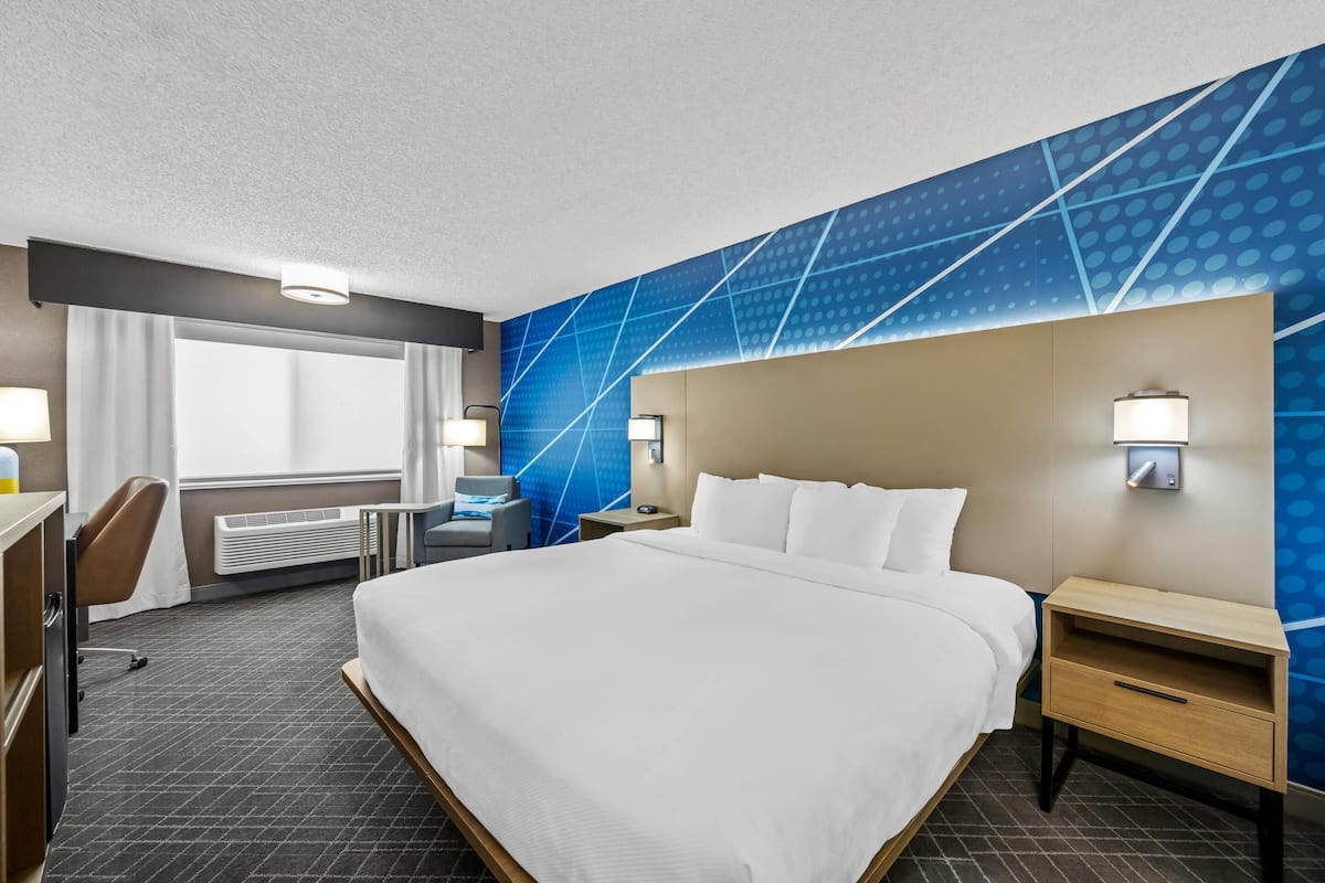 Hotelkamer met een groot bed, een bureau, een stoel, een raam met gordijnen en een muur met een geometrisch patroon.