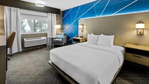 A hotel room with a large bed, a desk, a chair, a small table, and a wall-mounted heater. - Comfort Inn Grand Junction I-70 (Grand Junction)