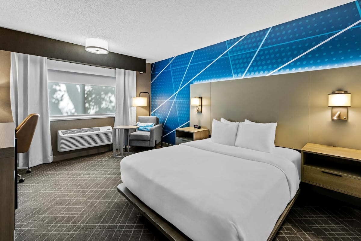 Een hotelkamer met een groot bed, een bureau, een stoel, een bijzettafeltje en een wandradiator.