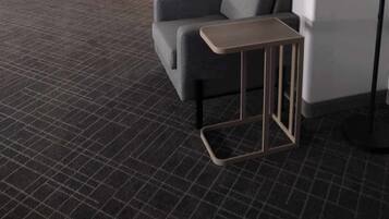 Una sala de estar moderna con un sofá gris, un otomano amarillo, un sillón gris y una pequeña mesa de madera.