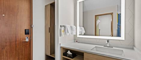 Un baño moderno con puerta de madera, un lavabo blanco, un espejo grande y un toallero.