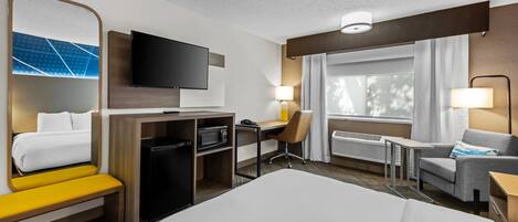 A hotel room with a bed, a desk with a chair, a television, a microwave, a small table, and a sofa.