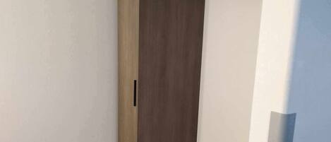 A walk-in closet with a wooden door, a black handle, and a black rod for hanging clothes.