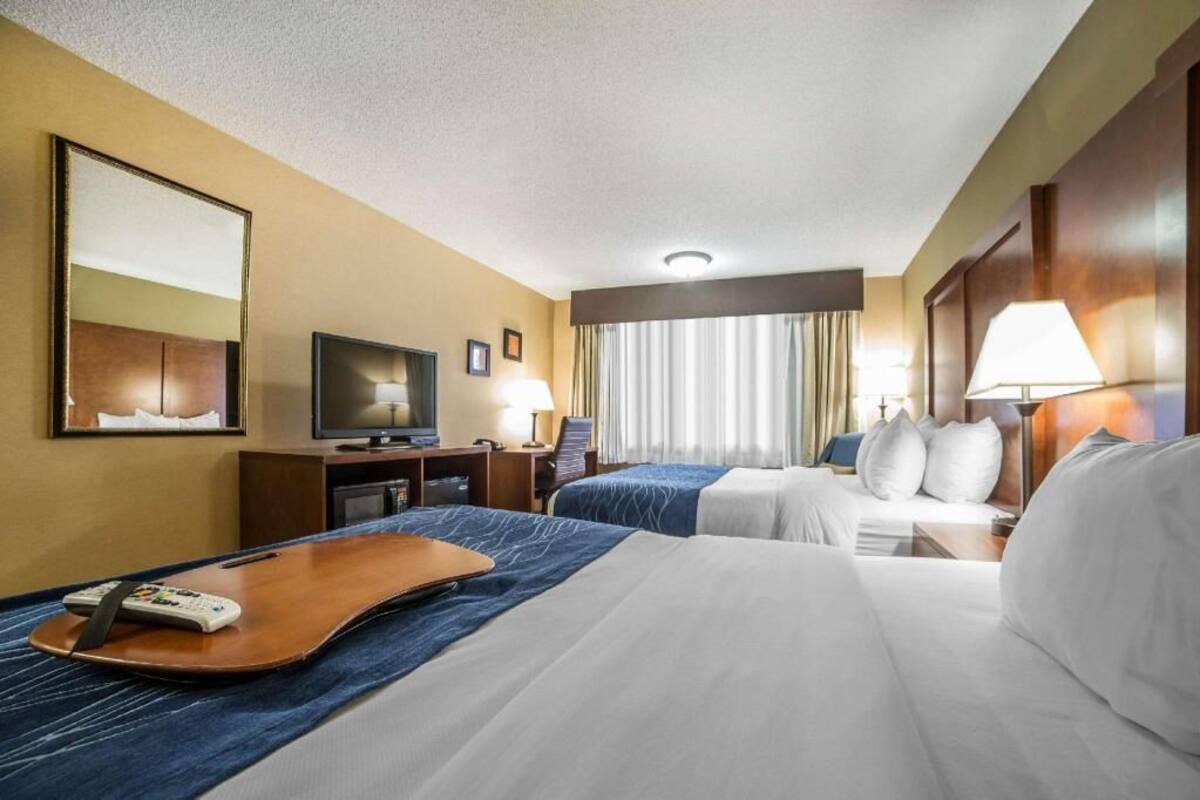A hotel room with two beds, a TV, a desk with a lamp, and a window with curtains.