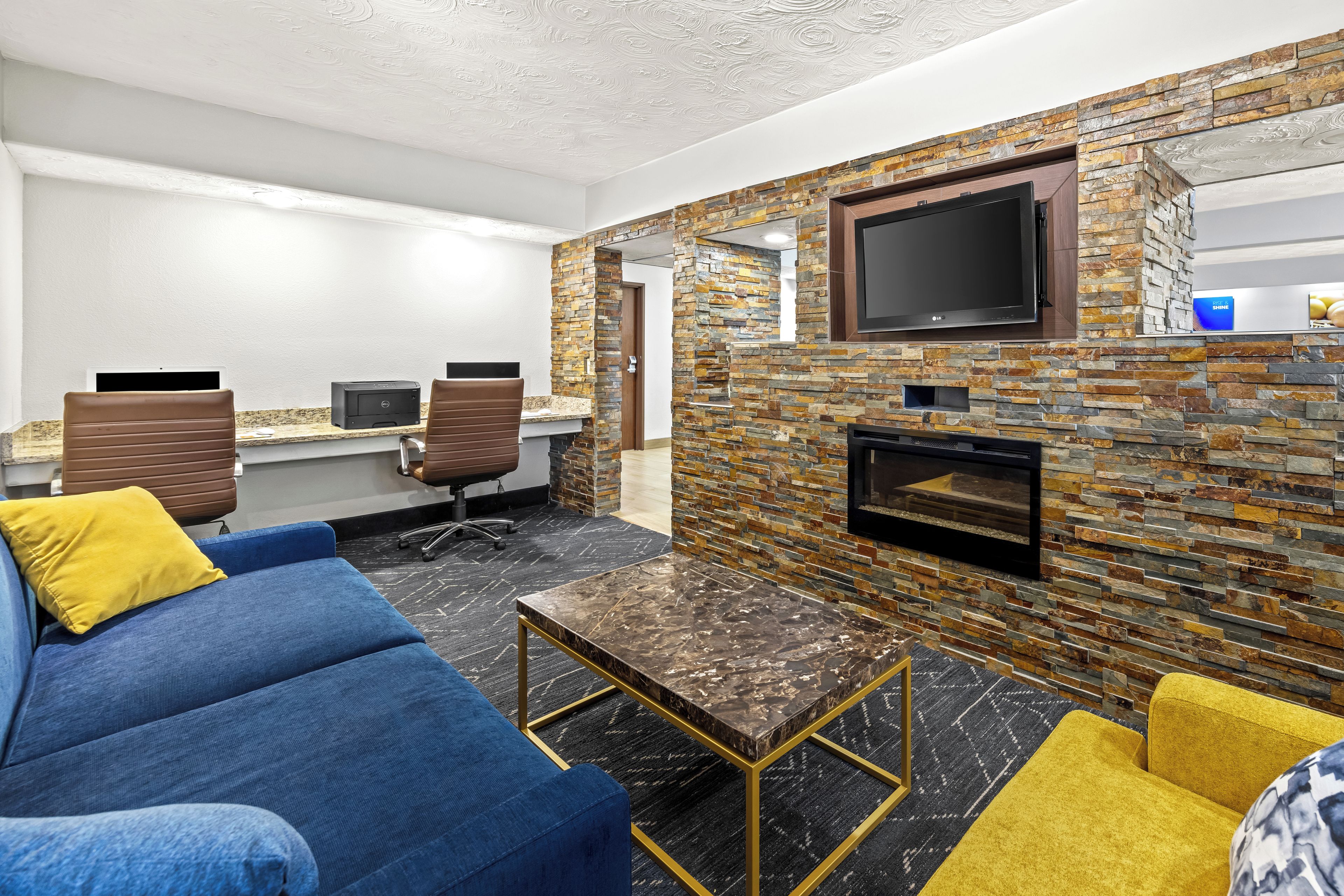 A modern lounge area with a blue sofa, yellow cushions, a marble coffee table, and a stone wall with a flat-screen TV.