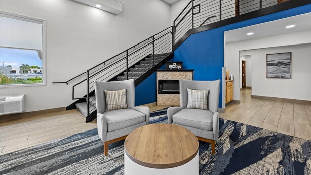 A spacious living area with a staircase, two grey armchairs, a round coffee table, and a view of the outside. - Comfort Inn Grand Junction I-70 (Grand Junction)