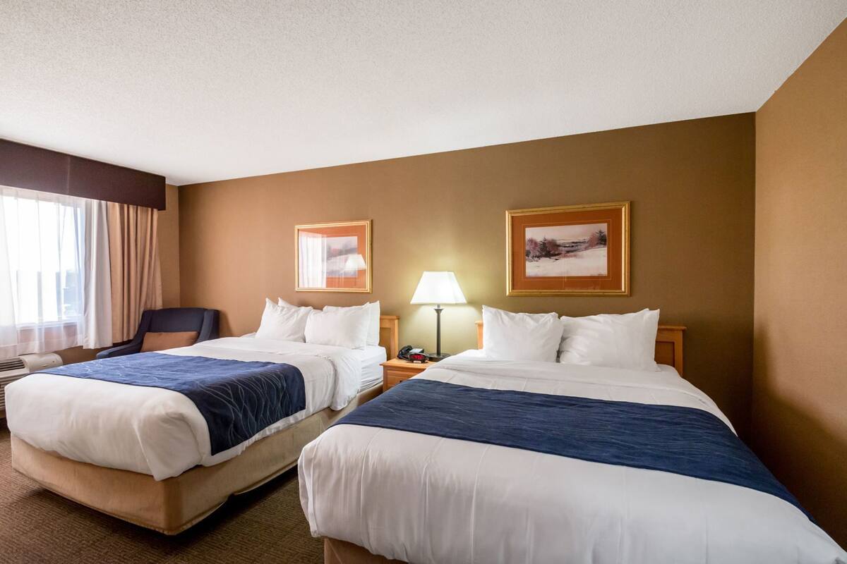 A hotel room with two beds, a desk, a chair, and two framed pictures on the wall.