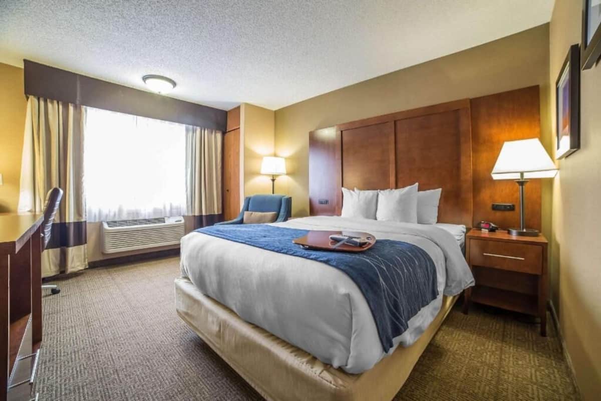 Een hotelkamer met een bed, nachtkastjes, een bureau, een stoel, een airconditioning en een raam met gordijnen.