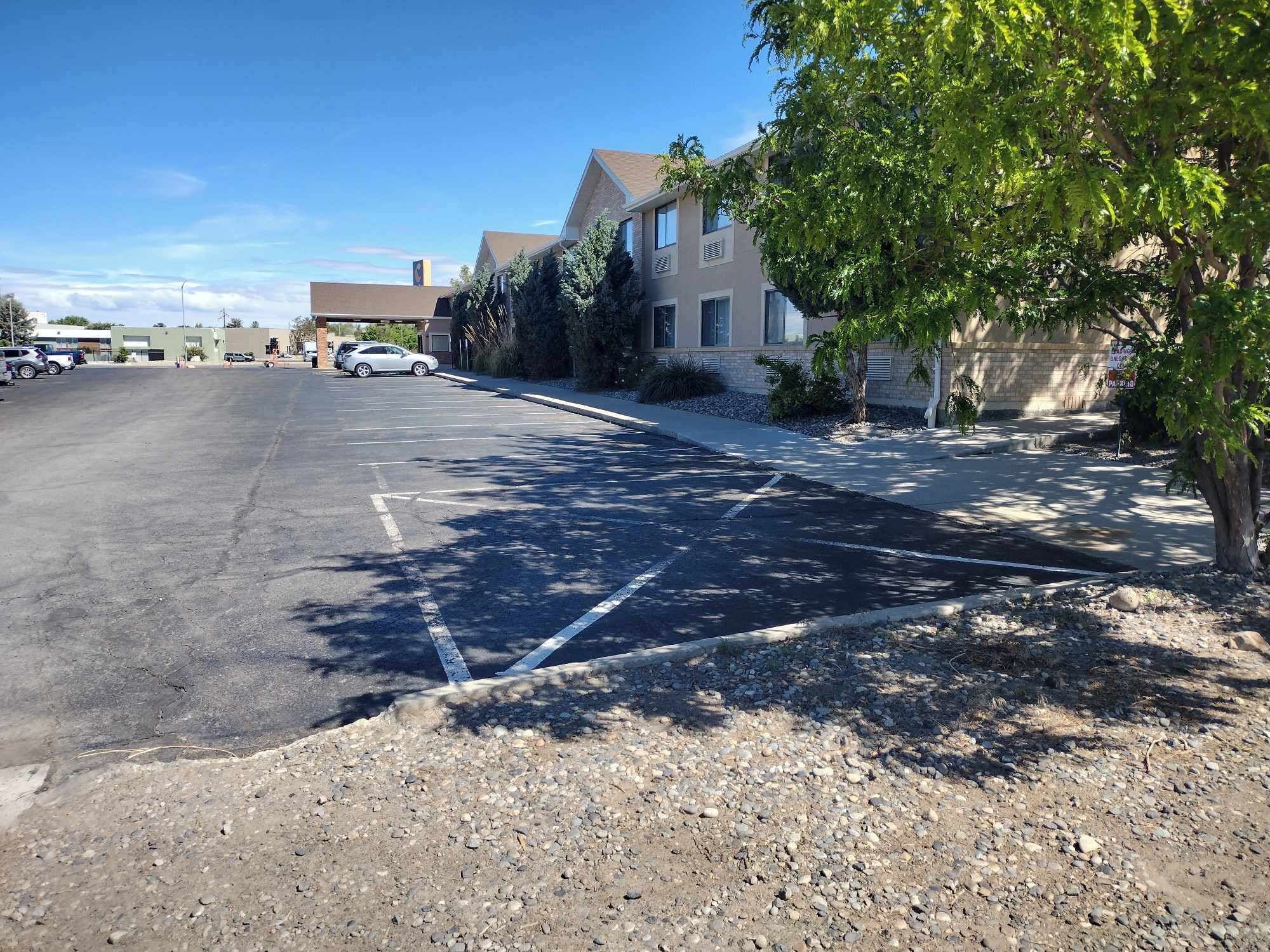 A parking lot with marked spaces, a building with a sloped roof, and a tree on the right.