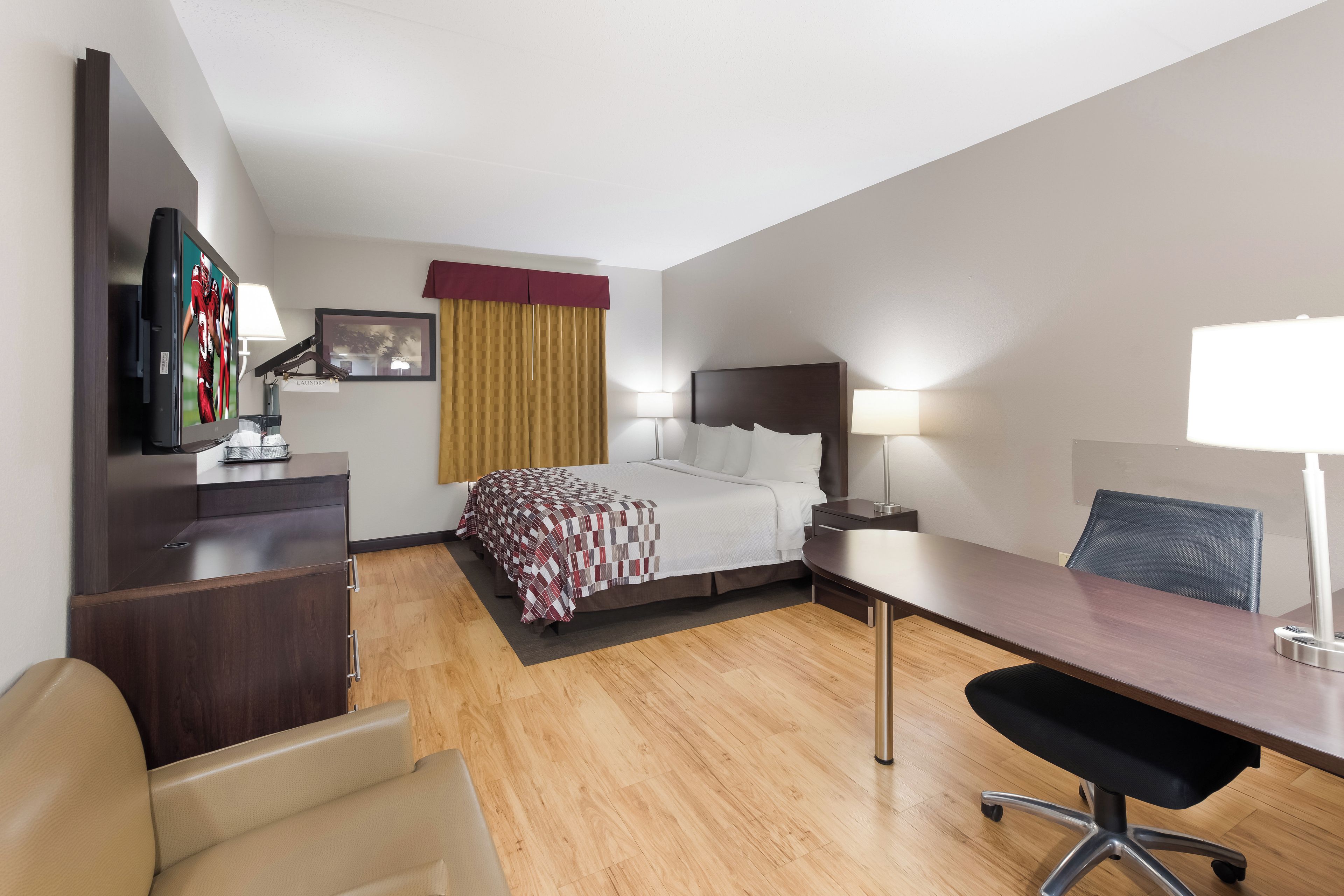 A hotel room with a bed, desk, chair, TV, and bedside lamps.