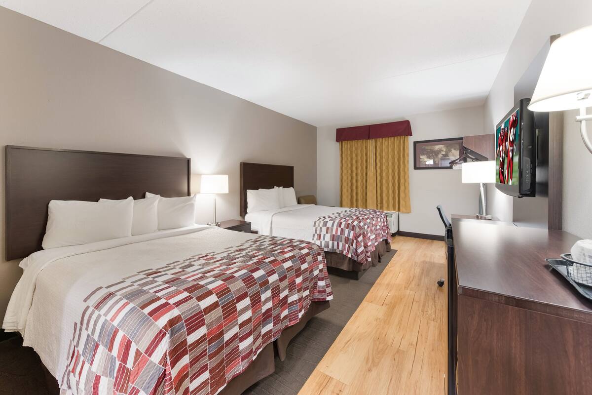 A hotel room with two beds, a desk, a television, and a window with curtains.
