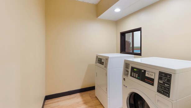 A laundry room with two stacked washers and dryers, a wooden floor, and a ceiling light. - Red Roof Inn & Suites Columbus - West Broad (Columbus)