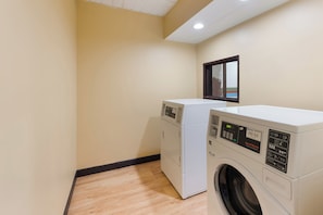 Une buanderie équipée de deux machines à laver et deux sèche-linge superposés, avec un plancher en bois et un luminaire au plafond.