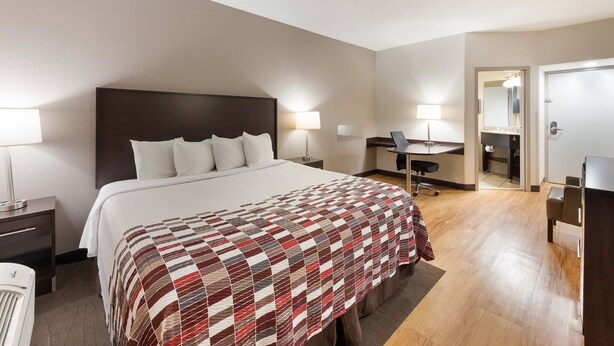 A hotel room with a large bed, a desk, a chair, and a mirror. - Red Roof Inn & Suites Columbus - West Broad (Columbus)