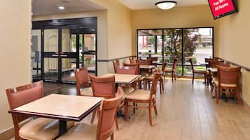 Un restaurante con mesas y sillas, vista al exterior y un cartel que indica conexión Wi-Fi gratuita.
